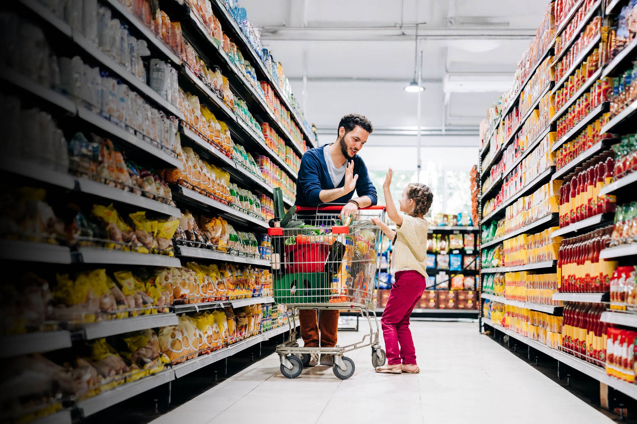 Girl giving high five to father at aisle. Young man and daughter are shopping in grocery store. They are in supermarket.