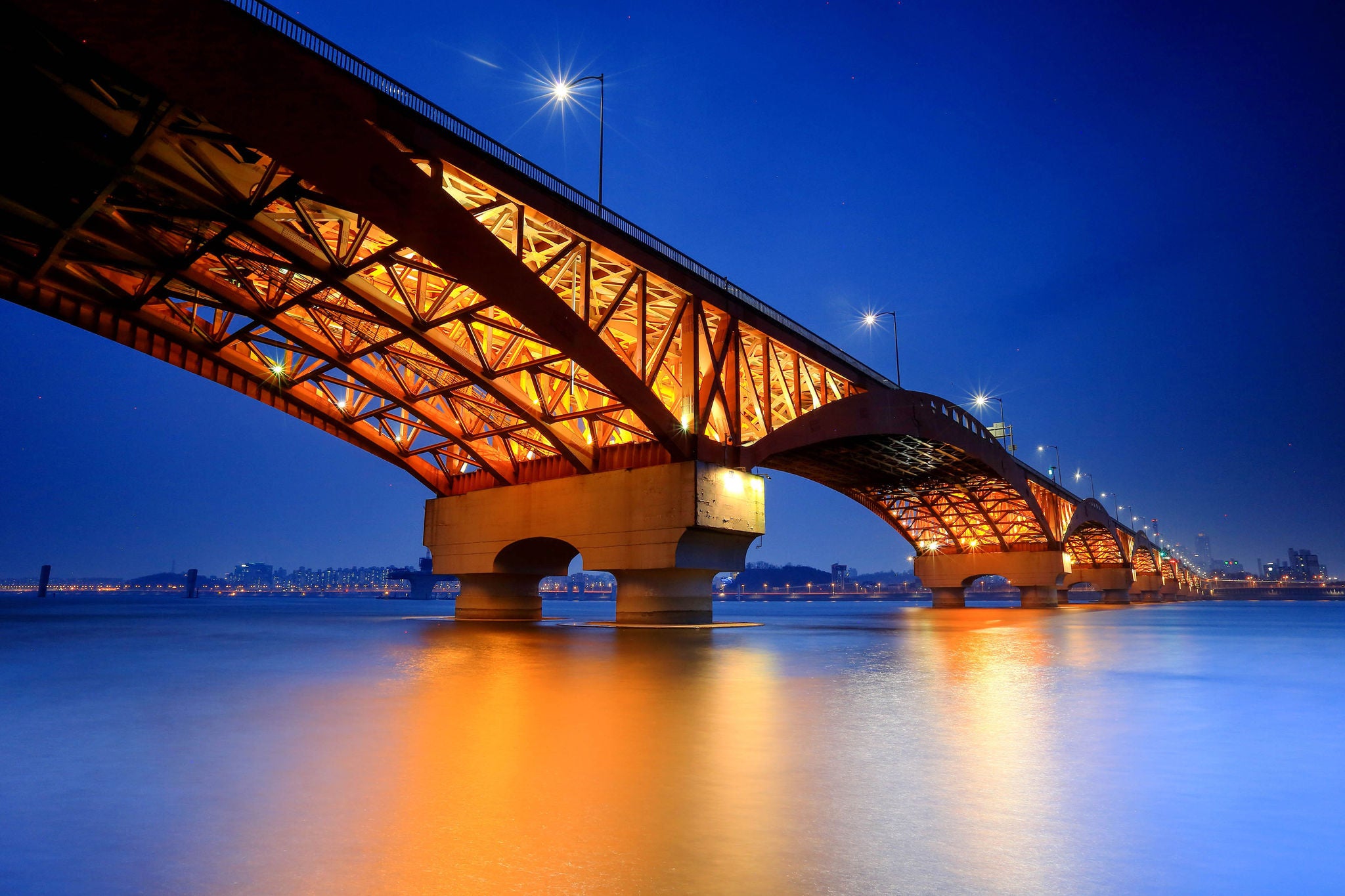 ILLUMINATED BRIDGE OVER RIVER AGAINST SKY AT NIGHT