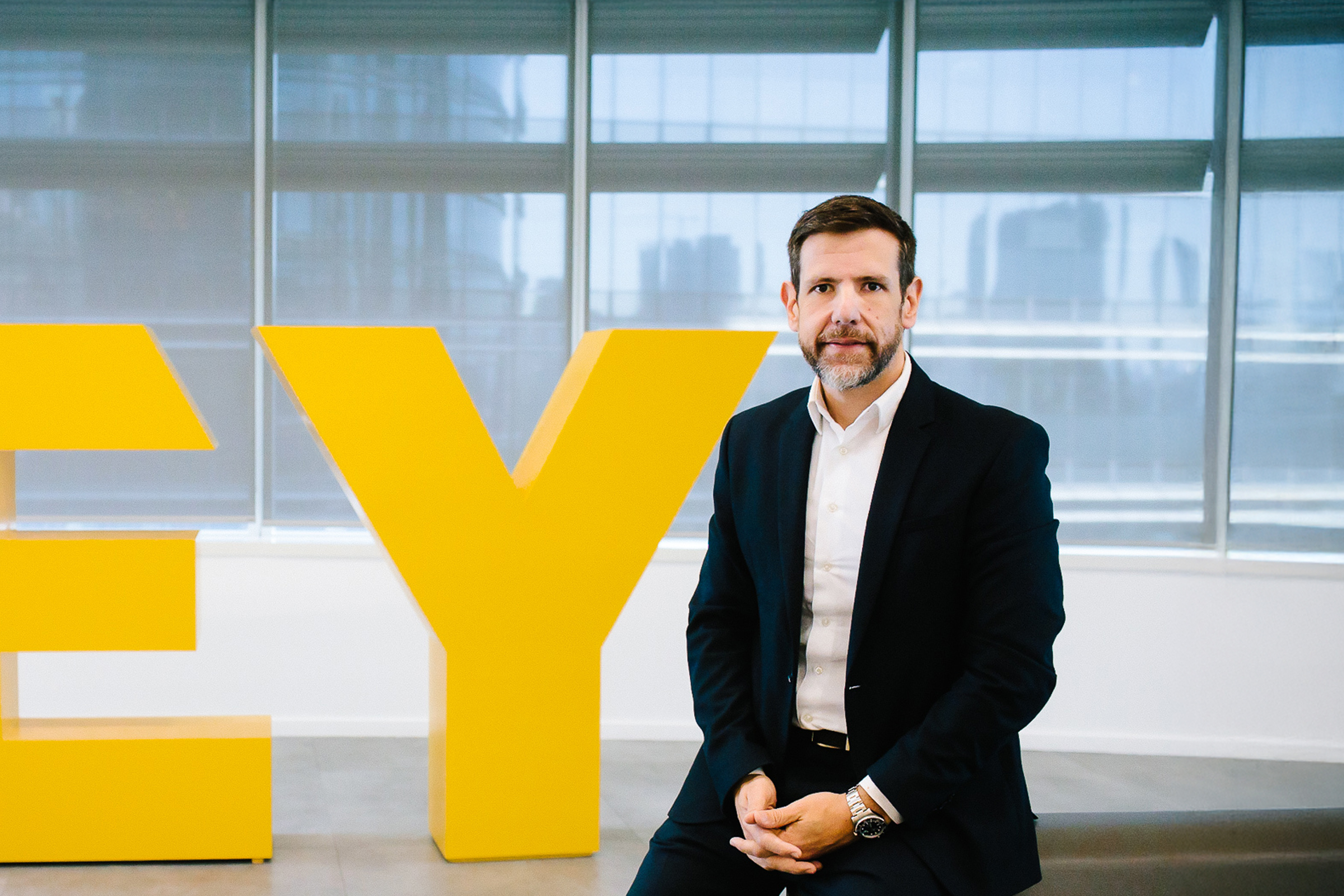 Ricardo Assumpção em fotografia ao lado do Logo da EY